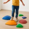 Sechs Bunte Balanciersteine auf Holzboden. Ein Kind balanciert darauf.