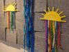 Drei gebastelte gelbe Sonnen aus Papptellern mit buntem Kreppband welches einen Regenbogen darstellen soll